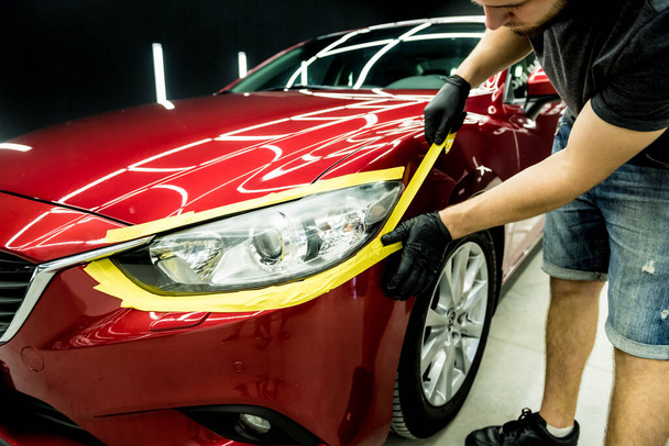 Car service worker applying protective tape on the car details before polishing. - Fotoğraf, Görsel