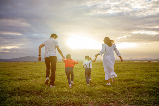 Ázsiai család sétál és fut a réten naplementekor boldog érzelmekkel. Családi, üdülési és utazási koncepció. - Fotó, kép