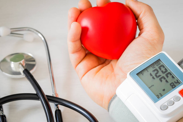 Manometer. Blutdruck messen und Herzfrequenz untersuchen, Stethoskop. Eine Hand umklammert ein Gummiherz. - Foto, Bild