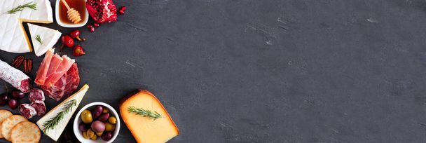 Různé druhy sýrů a masových předkrmů. Horní okraj zobrazení rohu na tmavém břidlicovém pruhu na pozadí s kopírovacím prostorem. - Fotografie, Obrázek