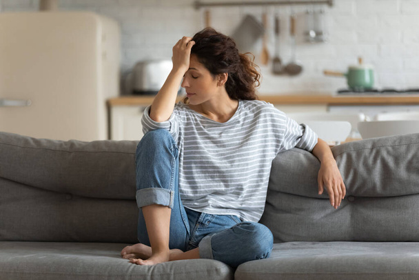 Exhausted frustrated young woman touching forehead, sitting on couch alone - Foto, Bild