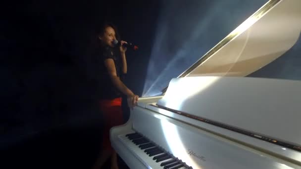sexy cantante chica con micrófono caminando en el escenario alrededor del piano, rendimiento. - Metraje, vídeo