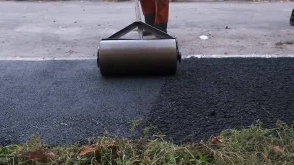 De werknemer duwt een handmatige roller voor asfalt bestrating van de stoep.. Wegenwerken close-up - Video