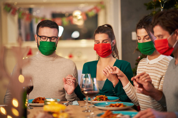 Gruppe von Freunden in Masken betet zu Hause über den Weihnachtstisch - Foto, Bild