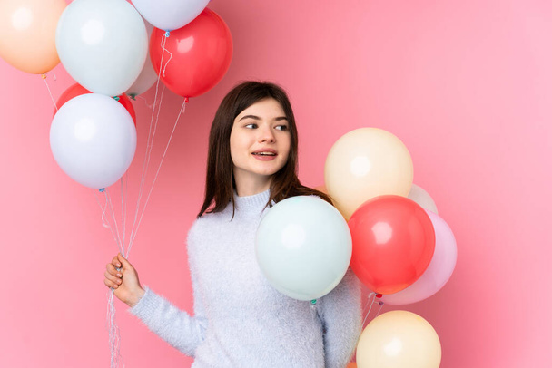 Young Ukrainian teenager girl holding lots of balloons over isolated pink background - Zdjęcie, obraz