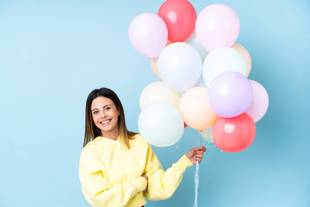 Frau hält Luftballons in einer Party über isoliertem blauem Hintergrund und schaut zur Seite - Foto, Bild