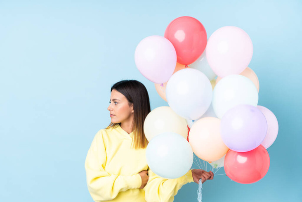 Woman holding balloons in a party over isolated blue background looking side - Photo, Image