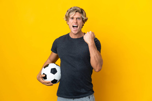 Hombre inglés sobre fondo amarillo aislado con pelota de fútbol celebrando una victoria - Foto, imagen