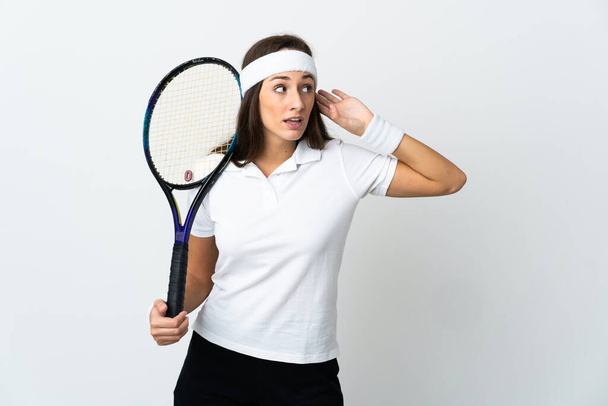 Młoda kobieta tenisistka na odizolowanym białym tle słuchając czegoś, kładąc rękę na uchu - Zdjęcie, obraz