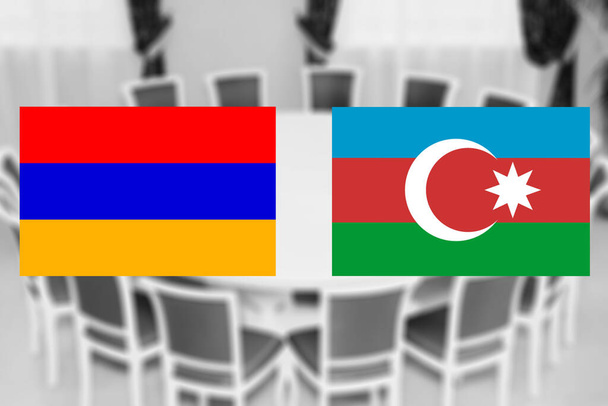 円形のテーブルの背景にアゼルバイジャンとアルメニアの旗。敵対行為の停止に関する戦争当事者や外交交渉の休戦 - 写真・画像
