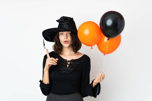 Giovane strega che tiene palloncini d'aria neri e arancioni con l'intenzione di realizzare la soluzione mentre solleva un dito - Foto, immagini
