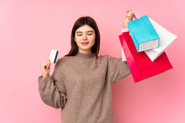 Joven adolescente ucraniano sobre fondo rosa aislado sosteniendo bolsas de compras y una tarjeta de crédito - Foto, Imagen