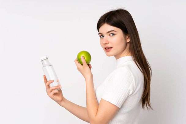 Young Ukrainian teenager girl over isolated white background with an apple and with a bottle of water - Fotografie, Obrázek