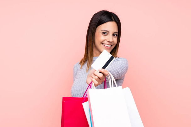 Mujer sobre fondo rosa aislado sosteniendo bolsas de compras y una tarjeta de crédito - Foto, imagen