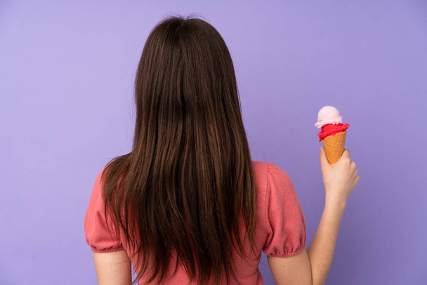 Young Ukrainian teenager girl holding a cornet ice cream over isolated purple background in back position - Photo, Image