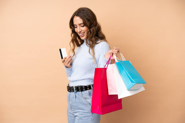 Молодая женщина на изолированном фоне держит сумки с покупками и кредитную карту - Фото, изображение