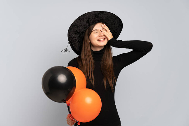 Siyah ve turuncu hava balonları tutan genç cadı çok gülümsüyor. - Fotoğraf, Görsel