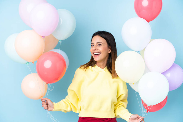 Frau hält Luftballons auf einer Party vor isoliertem blauen Hintergrund - Foto, Bild