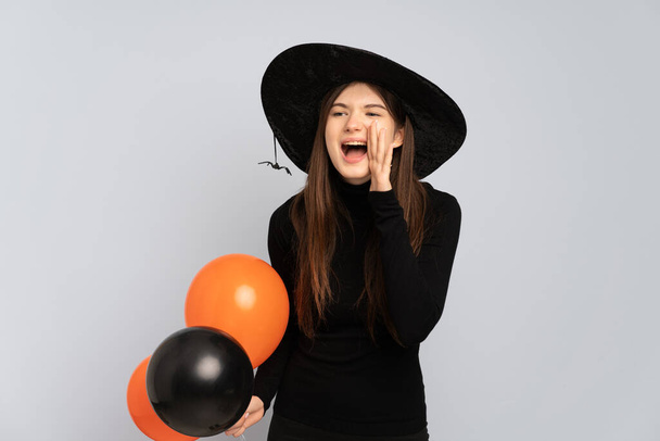 Νεαρή μάγισσα κρατώντας μαύρα και πορτοκαλί μπαλόνια αέρα φωνάζοντας με το στόμα ορθάνοιχτο στο πλάι - Φωτογραφία, εικόνα