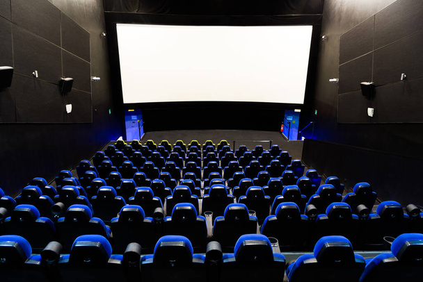 Interiér kina s obrazovkou a modrými sedadly. Široký pohled zezadu na prázdné hlediště se světly na stock fotografii - Fotografie, Obrázek