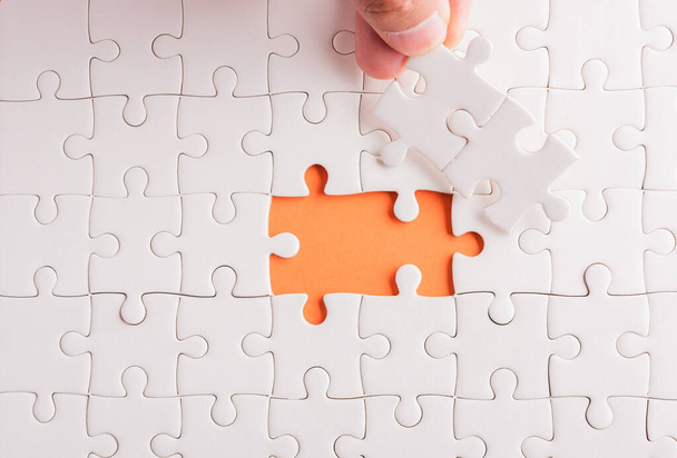 Top view flat lay of hand-holding last piece white paper jigsaw puzzle game last pieces put to place for solve problem complete mission, studio shot on an orange background, quiz calculation concept - Φωτογραφία, εικόνα