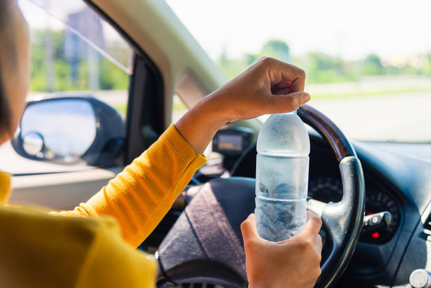 Asian woman holding a water bottle for drink while driving the car in the morning during going to work on highway road, Transportation and vehicle concept - Fotó, kép