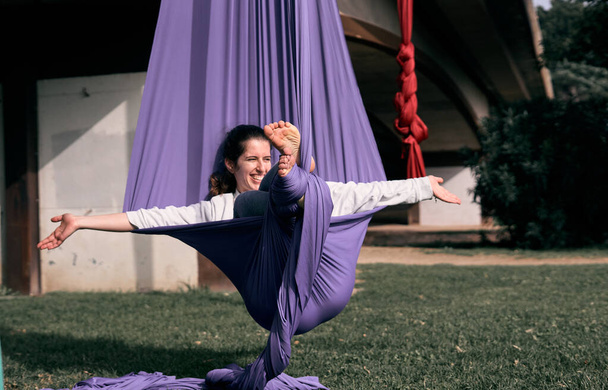 A happy Caucasian woman using her aerial stretch fabric as a hammock while practicing in a park - Foto, Bild