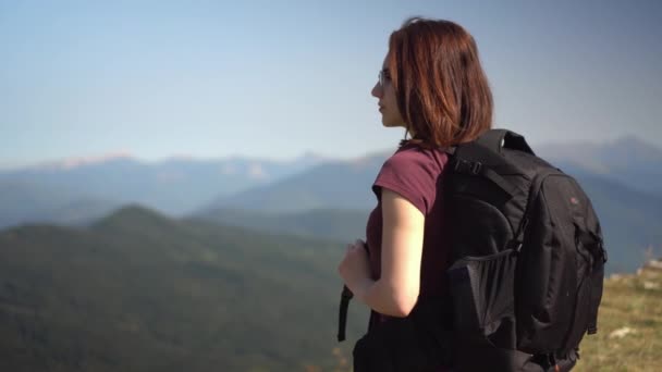 jonge vrouw in bril met een rugzak kijkt naar de bergketen. - Video