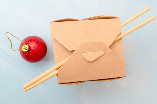 A closed WOK paper box with chopsticks and shiny red Christmas ball - Fotografie, Obrázek