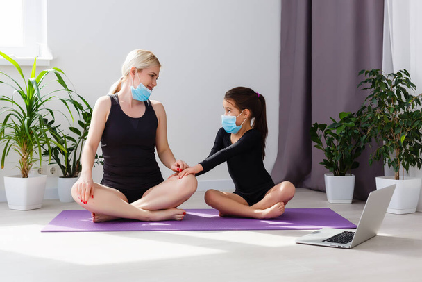 Thuis fitness. moeder en dochter doen yoga online thuis tijdens zelfisolatie quarantaine. COVID-19 concept om veilig thuis te blijven  - Foto, afbeelding