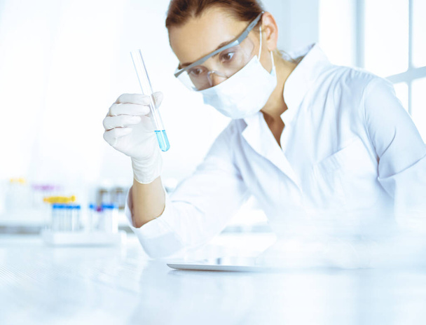 Female laboratory assistant analyzing test tube with blue liquid. Medicine, health care and researching concept - Foto, imagen