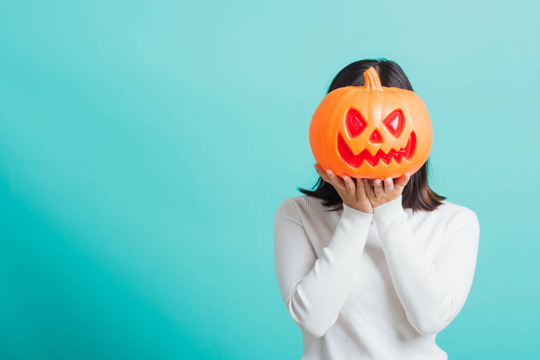 Portrait of Asian beautiful young woman holding orange model pumpkins at her head, funny happy female with ghost pumpkins, studio shot isolated on blue background - Foto, immagini