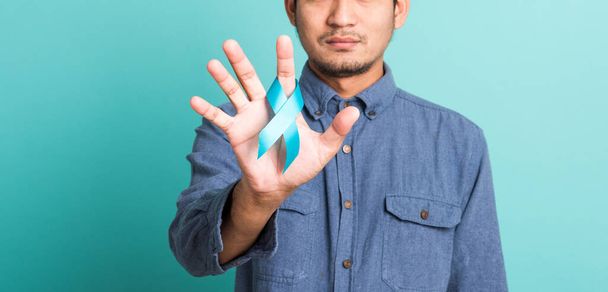 Asian portrait happy handsome man posing he holding light blue ribbon for supporting people living and illness, studio shot isolated on blue background, Prostate Cancer Awareness in November concept - Foto, imagen