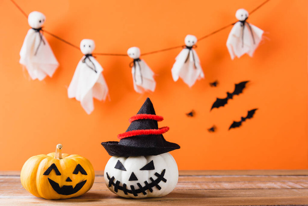 Funny Halloween day decoration party, Cute pumpkin ghost spooky jack o lantern face wear hat, black spider and bats on wooden table, studio shot isolated on an orange background, Happy holiday concept - Foto, imagen