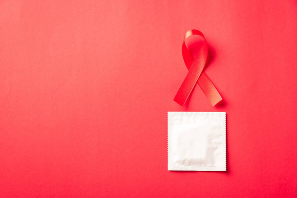 Red bow ribbon symbol HIV, AIDS cancer awareness and condom with shadows, studio shot isolated on red background, Healthcare medicine sexually concept, World AIDS Day - Photo, Image