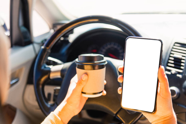 Asian woman drinking hot coffee takeaway cup inside a car and using smartphone blank screen while driving the car in the morning during going to work on highway, Transportation and vehicle concept - Zdjęcie, obraz