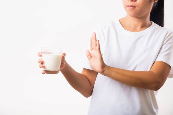 Closeup woman raises a hand to stop sign use hand holding glass milk she is bad stomach ache has bad lactose intolerance unhealthy problem with dairy food, studio shot isolated on white background - Photo, image