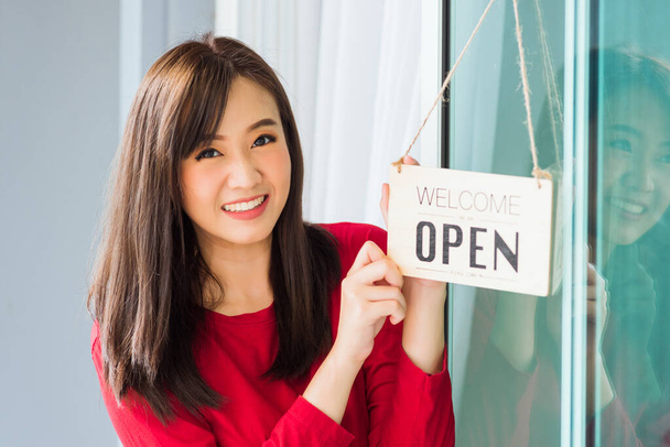 Asian young woman glad and smiling she notice sign wood board label "WELCOME OPEN" hanging through glass door front shop, Business turning open after coronavirus pandemic disease, back to new normal - Photo, Image