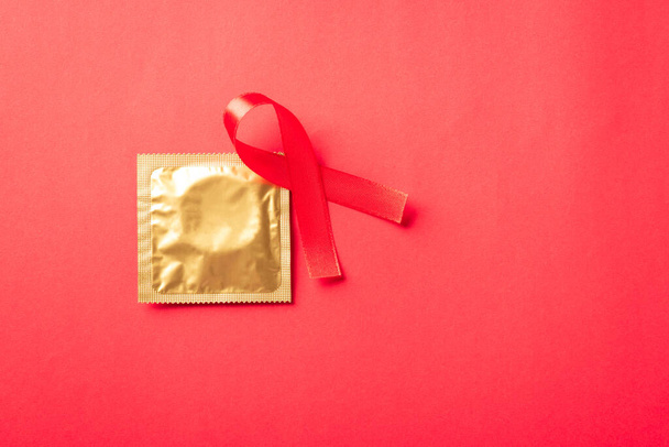 Red bow ribbon symbol HIV, AIDS cancer awareness and condom with shadows, studio shot isolated on red background, Healthcare medicine sexually concept, World AIDS Day - Фото, зображення