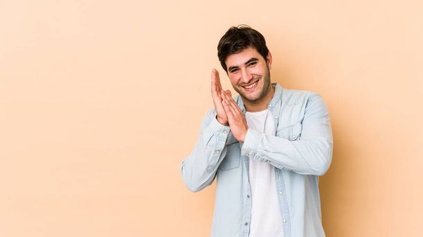 Young man isolated on beige background feeling energetic and comfortable, rubbing hands confident. - Foto, Imagen