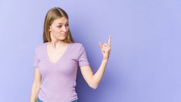 Jeune femme blonde isolée sur fond violet pointant du doigt vers vous comme si vous invitant se rapprocher. - Photo, image