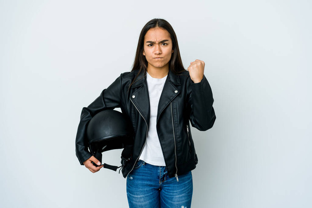 Joven mujer asiática sosteniendo un casco de moto sobre fondo aislado mostrando puño a cámara, expresión facial agresiva. - Foto, imagen