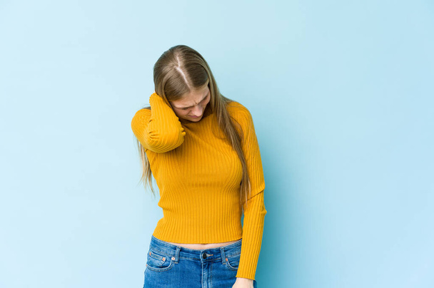 jonge blonde vrouw geïsoleerd op blauwe achtergrond met een nek pijn als gevolg van stress, masseren en aanraken van het met de hand. - Foto, afbeelding
