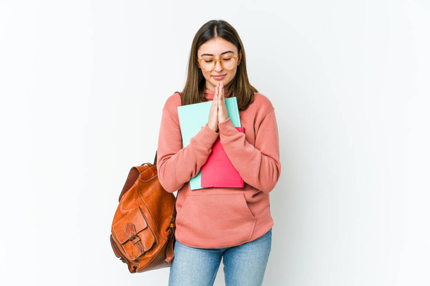 Giovane studentessa isolata su bakcground bianco tenendosi per mano in pregare vicino alla bocca, si sente fiducioso. - Foto, immagini