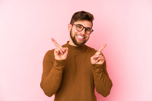 Junge kaukasische Mann isoliert auf rosa Hintergrund zeigt auf verschiedene Kopierräume, Auswahl eines von ihnen, zeigt mit dem Finger. - Foto, Bild