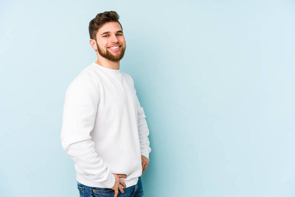 Young caucasian man isolated on blue background confident keeping hands on hips. - Photo, Image