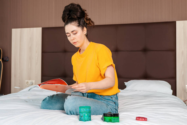 Μια νεαρή όμορφη γυναίκα κάθεται στο κρεβάτι και διαβάζει ένα περιοδικό. Στο σπίτι. Ανάγνωση και εκπαίδευση. - Φωτογραφία, εικόνα