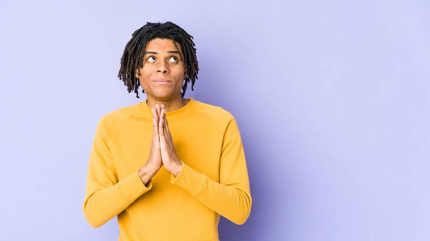 Young black man wearing rasta hairstyle holding hands in pray near mouth, feels confident. - Photo, image