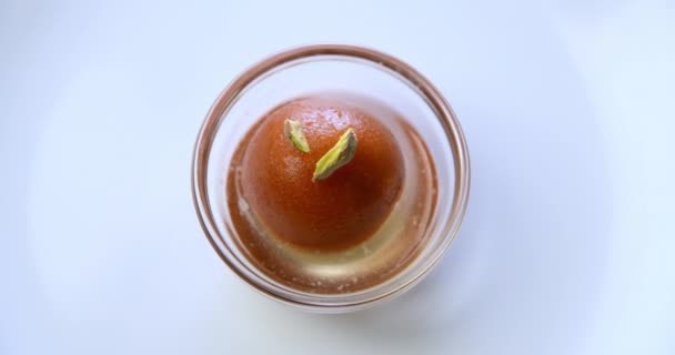 Top giratorio de gulab jamun con tapa de pistacho en cuenco de vidrio. Este es un plato dulce indio o postre - Imágenes, Vídeo