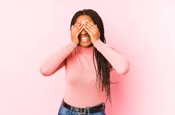 Young african american woman isolated on a pink background covers eyes with hands, smiles broadly waiting for a surprise. - Valokuva, kuva